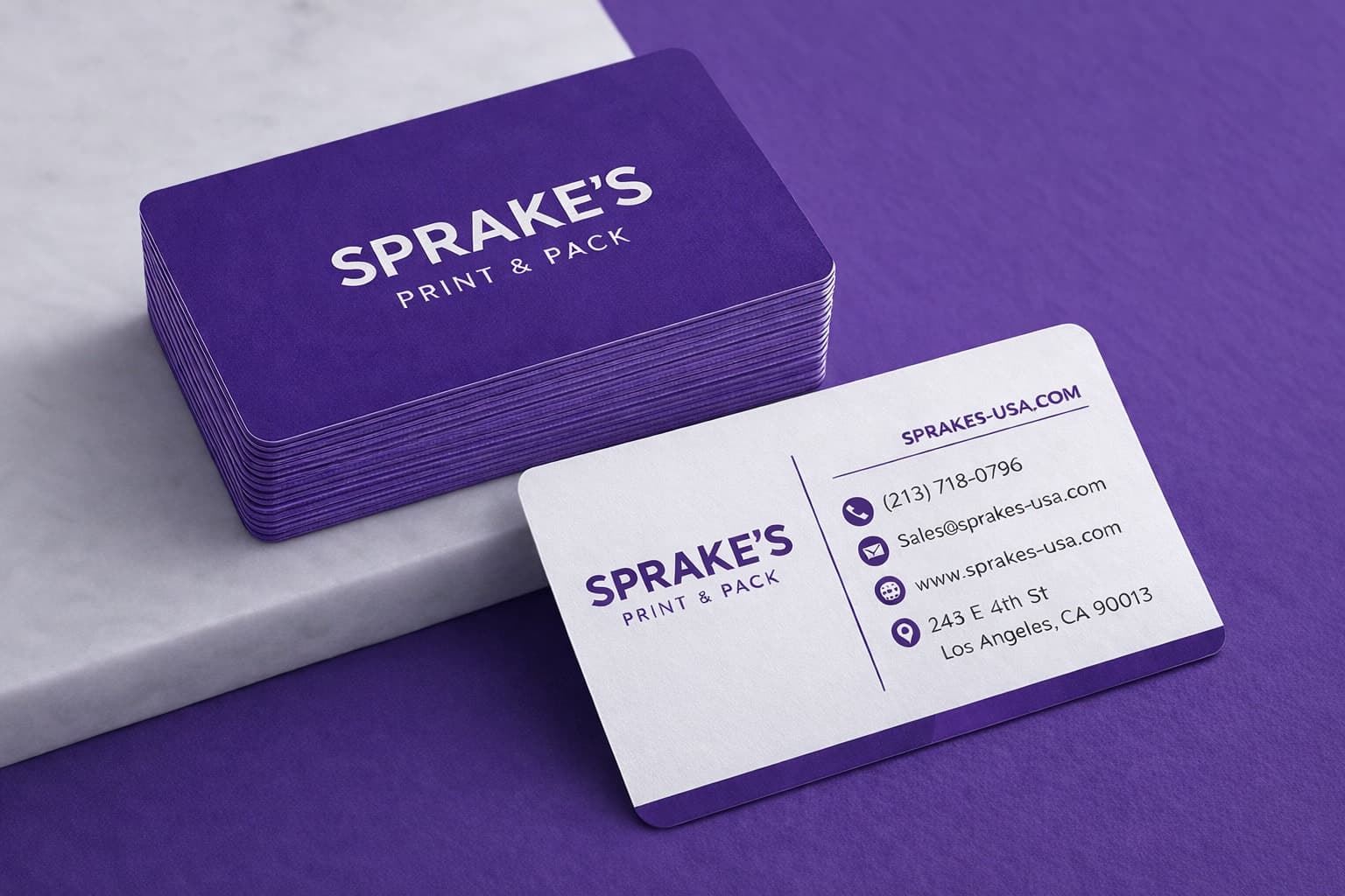 A stack of purple Sprake's Print & Pack business cards beside a white card showing the shop's phone, email, web address, and East 4th Street address