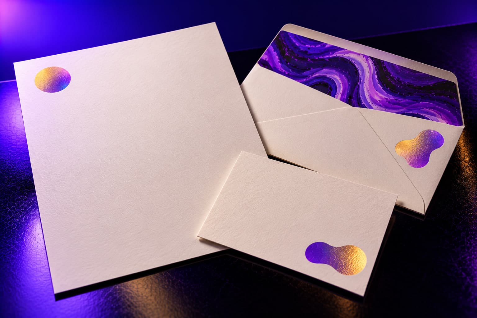 A letterhead sheet, a #10 envelope with printed flap, and a notecard arranged on a black surface, each with a foil mark